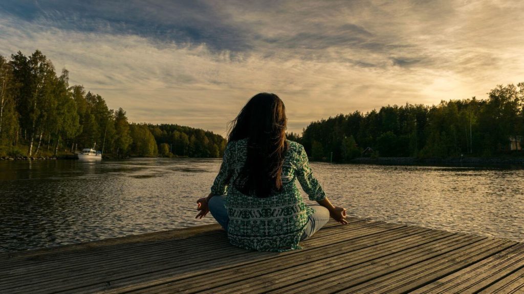 woman meditating on a deck at a lake