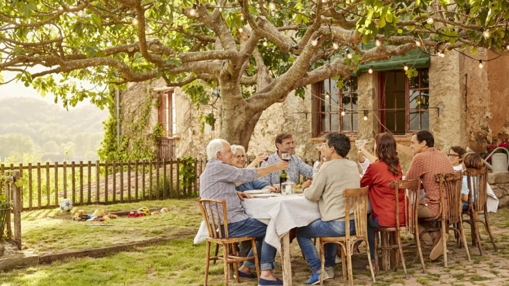 Multi-generational family having a toast whilst they sit down for a meal at an Italian vineyard.