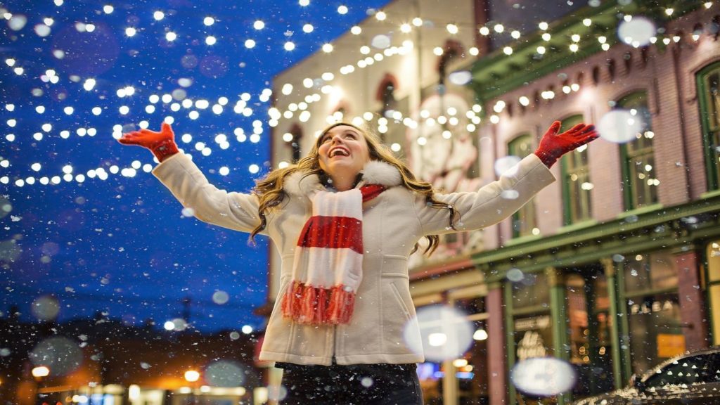 woman standing under snow and christmas lights smiling