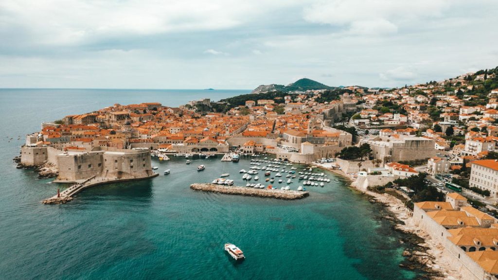 An aerial view of Dubrovnik's iconic walled city, its orange rooftops brightening up the deep blue Adriatic Sea.