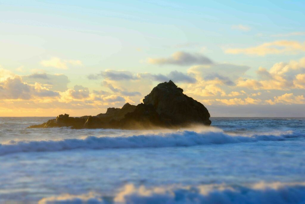 Cloud-filled sky, close-up of the California coastline in Big Sur. Large rock formations coming out of the coast.