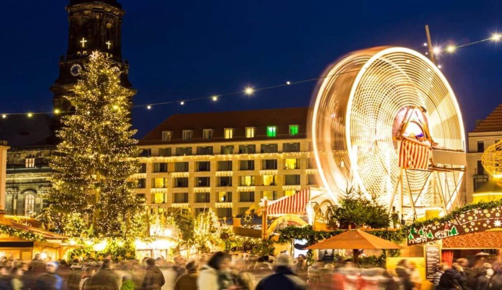 Christmas market with festive lights, a decorated tree, and a spinning ferris wheel at dusk, perfect for planning your Christmas vacation.