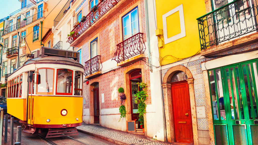 Yellow tram driving past colourful buildings in Lisbon, Portugal