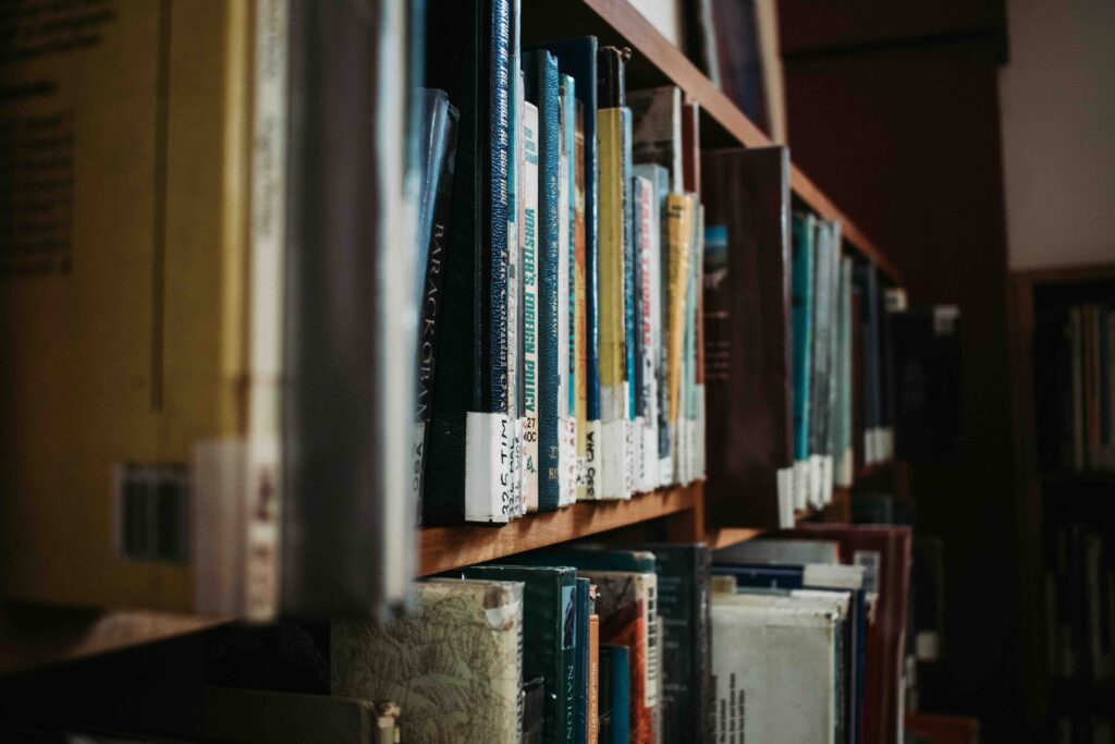 Close-up of a library bookshelf, the spines of the books are facing outwards. Brown bookshelf in a dark room.
