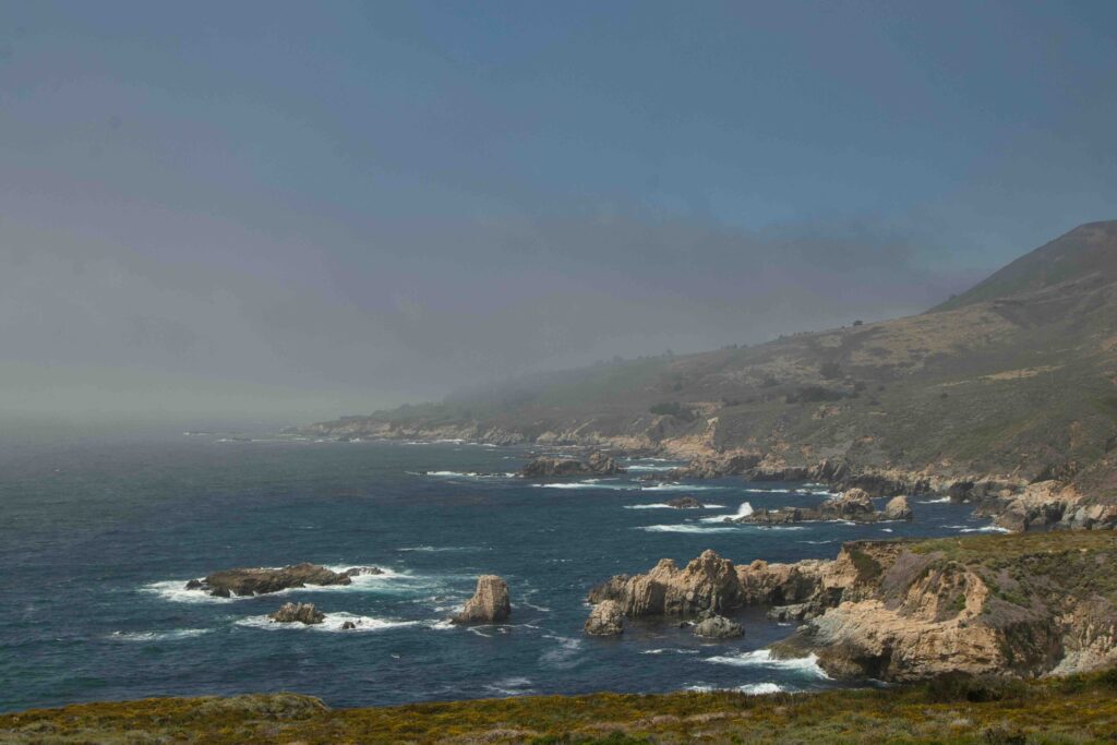 Foggy view from Big Sur, can see the blue water and rock formations coming out of the coastline.