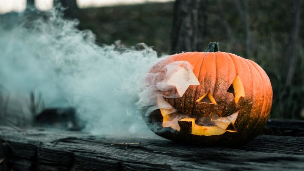A jack o' lantern set on a table, smoke fuming from its carved face.