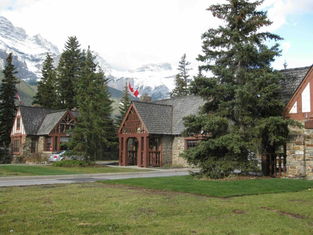 Banff National Park cabin's in the foreground, with trees outside the windows. In the backdrop, can see the snowy peaks of the mountain range.