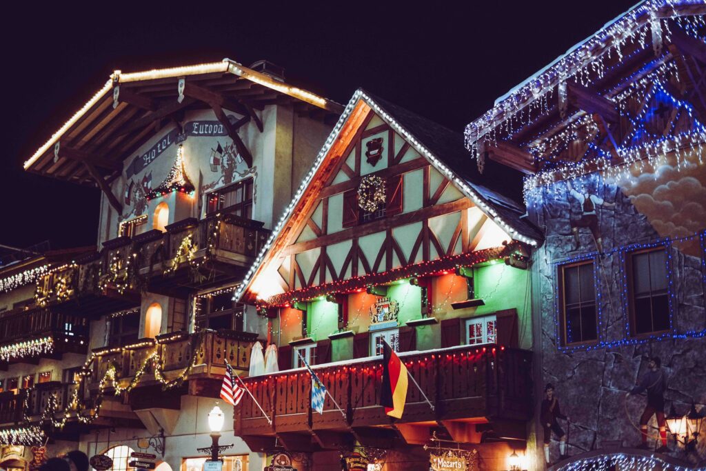 Close-up of three German-style buildings with balconies. German and US flag hanging from the middle building, along with another flag which is hidden. Buildings have Christmas lights on them.