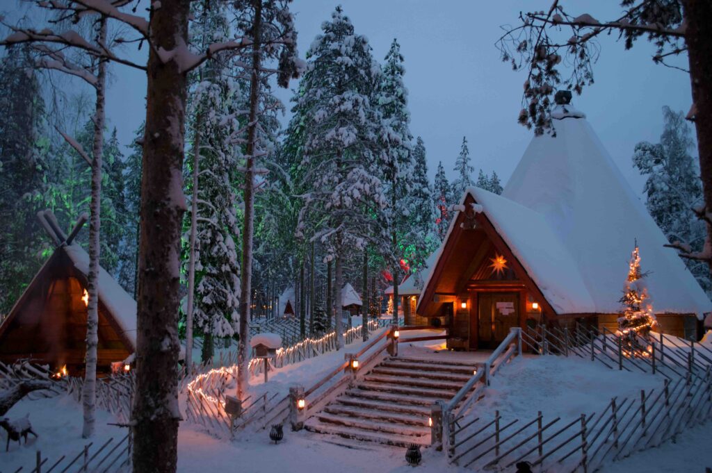 Two snowy-capped cabins in Rovaniemi, the hometown of Santa Claus. Steps leading up the big cabin in the center, with snow-filled trees surrounding it.