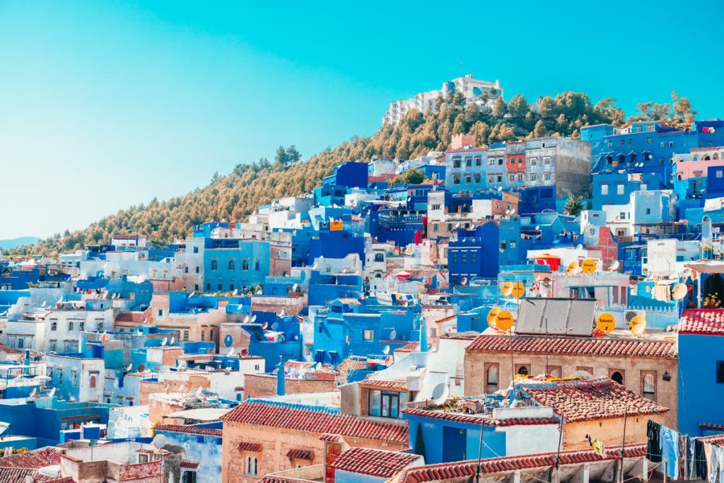 Vibrant blue and white buildings of Chefchaouen, the blue pearl city in Morocco, with a fortress on a hill in the background, make it an ideal place to visit when planning to