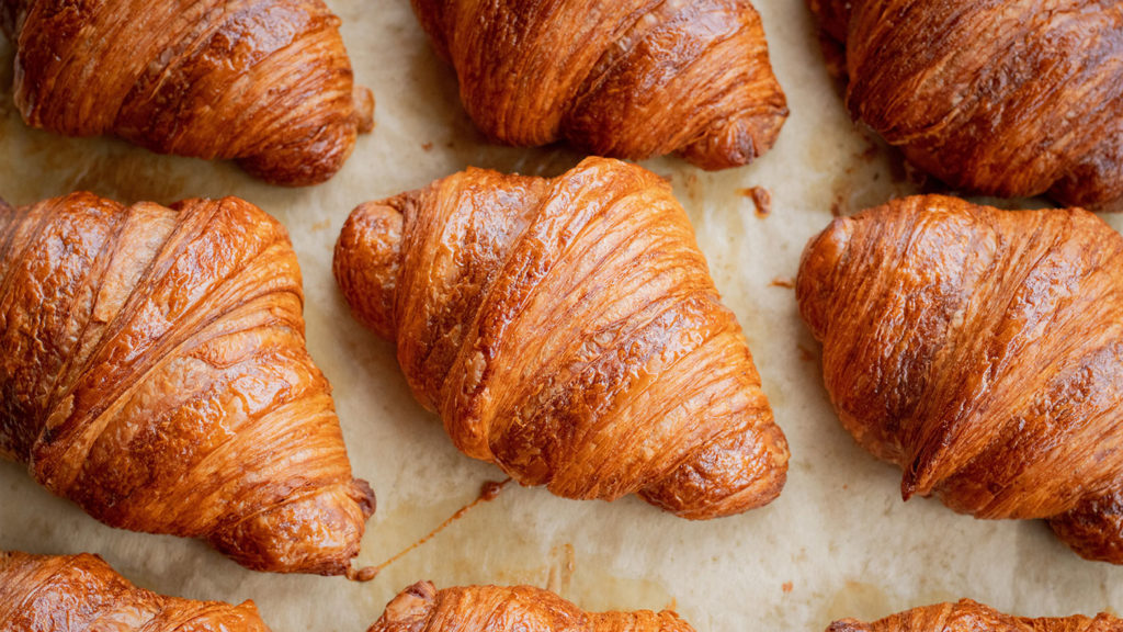 Freshly baked croissants, with a rich history of the croissant, on parchment paper.