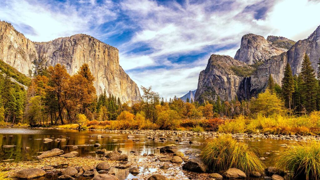 Scenic view of Yosemite Valley, one of the best national parks in the USA, with El Capitan and Bridalveil Fall, river in foreground, surrounded by autumn-colored trees under a cloudy