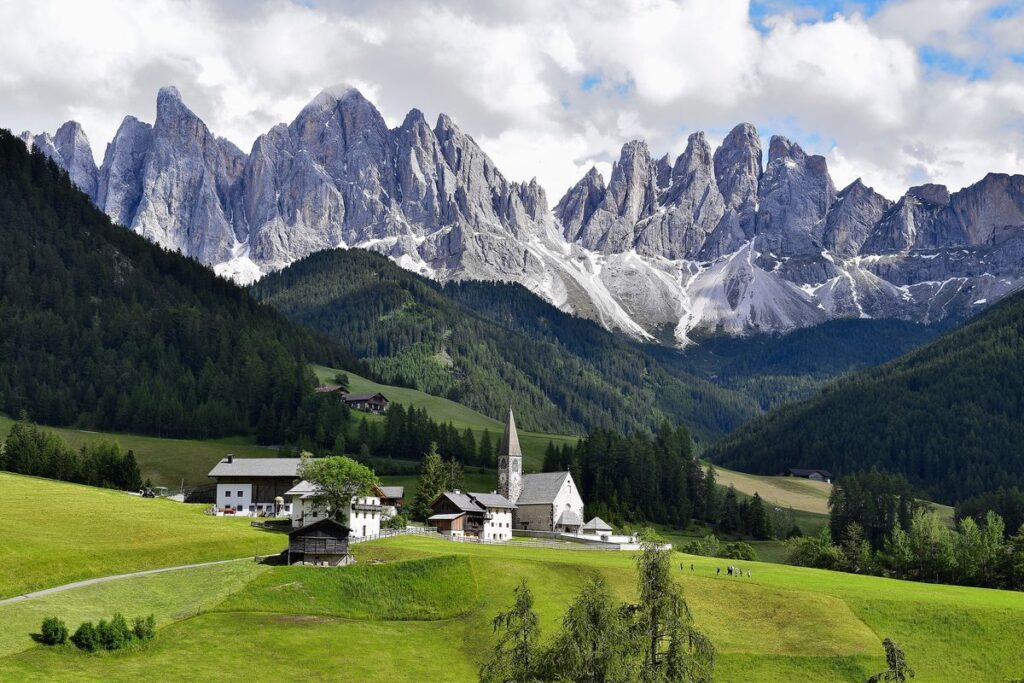 View of green meadows and a small Alpine commune with the jagged Dolomites in the background
