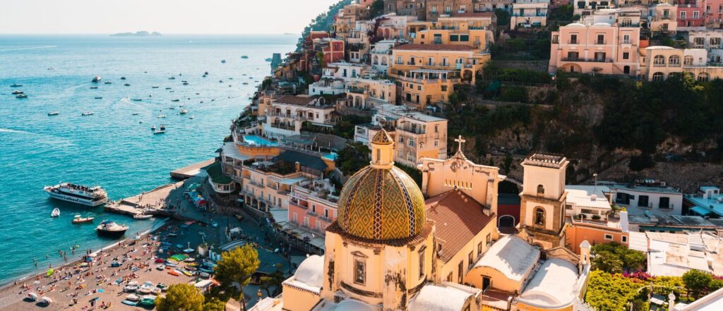 Aerial view of Positano's colorful cliffside houses overlooking the beach and boats in Italy's Mediterranean Sea.