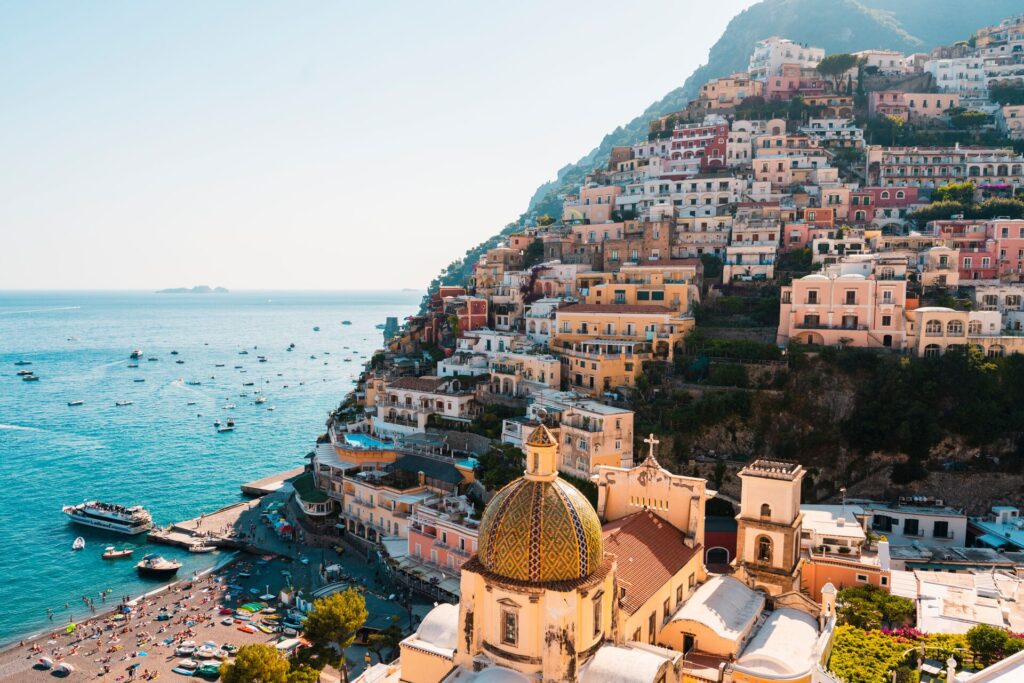 Aerial view of Positano, Italy, showcasing its colorful cliffside buildings and busy beachfront for a travel magazine, with boats in the water.