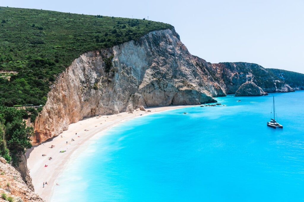 Aerial view of a stunning beach with turquoise waters, surrounded by high cliffs, featuring a few boats and visitors on the sand in September, the best month for travel.