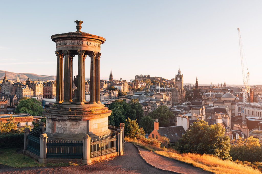Sunset view of Edinburgh with the Dugald Stewart Monument in the foreground overlooking the cityscape while travelling to Scotland in September.