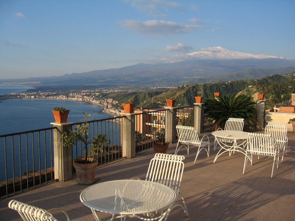 Taormina in Sicily, balcony with white chairs and tables spread throughout. Mount Etna is in the background.