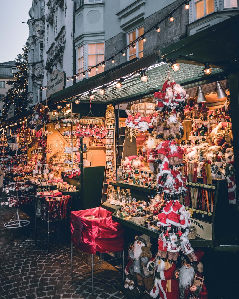 A festive outdoor Christmas market stall, reminiscent of the best Christmas Markets in Europe, decorated with lights and selling a variety of holiday ornaments and plush Santa Clauses.