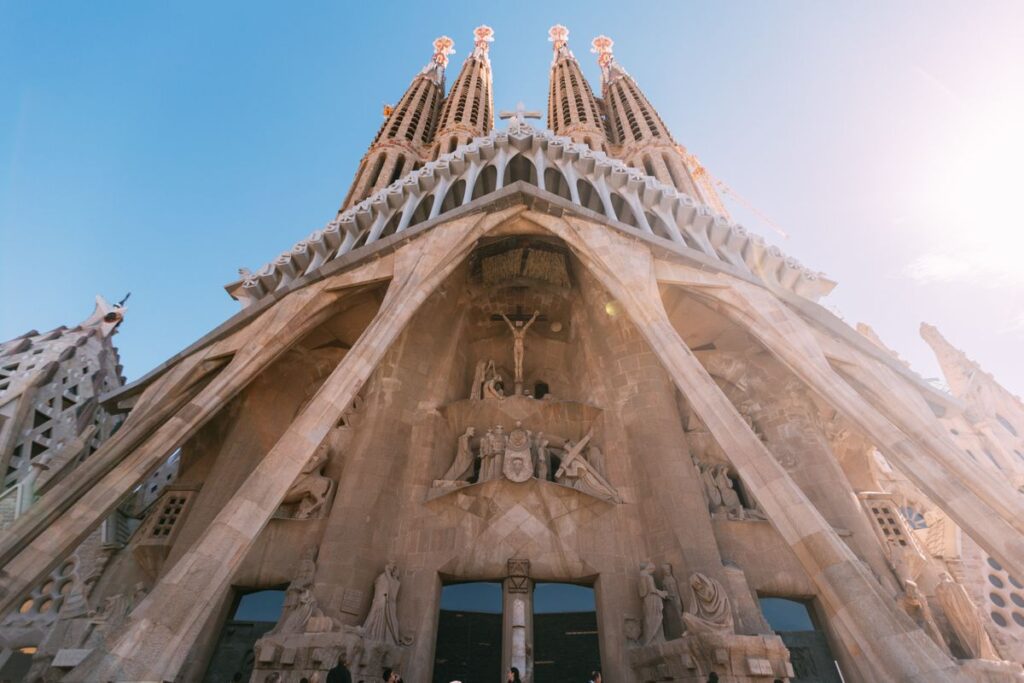 Low-angle view of the Sagrada Familia in Barcelona, showcasing its intricate facade and towering spires against a clear blue sky, a highlight among the best things to do in Barcelona.