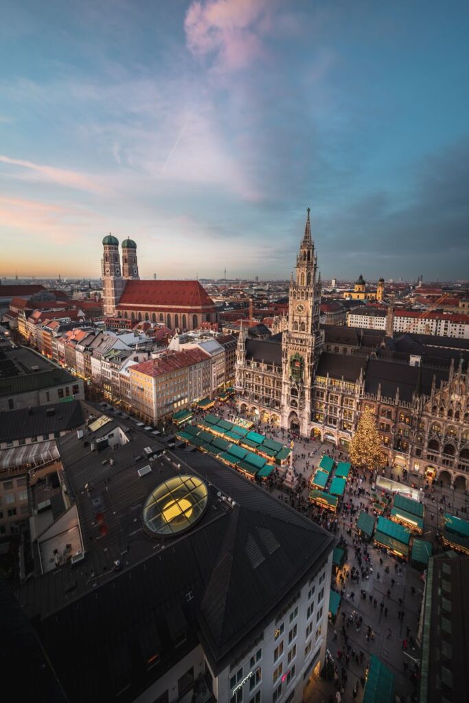 Aerial view of Marienplatz in Munich at dusk, showcasing the best Christmas Markets in Europe, the New Town Hall, bustling vendor stalls, and surrounding buildings.
