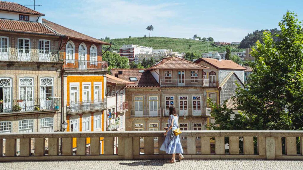 A woman stands on a bridge looking at beautiful colourful houses in the near distance