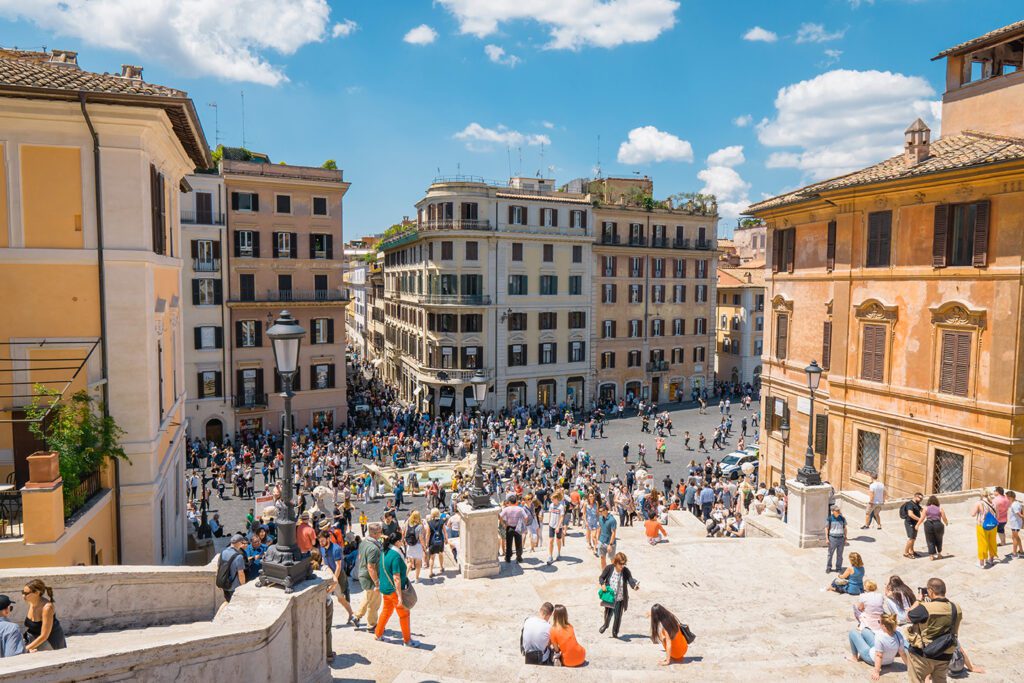 View of a busy square in Rome from a high vantage point, showing crowds of people and surrounding historic buildings outside of the summer season.