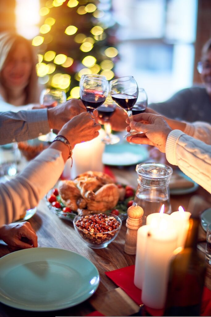 Group of friends toasting with red wine at a festive Canadian Thanksgiving dinner table decorated with a Christmas tree in the background.