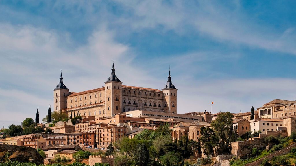 The alcázar of Toledo, a historic fortress located on a hill in Spain, overlooks the city under a clear blue sky.
