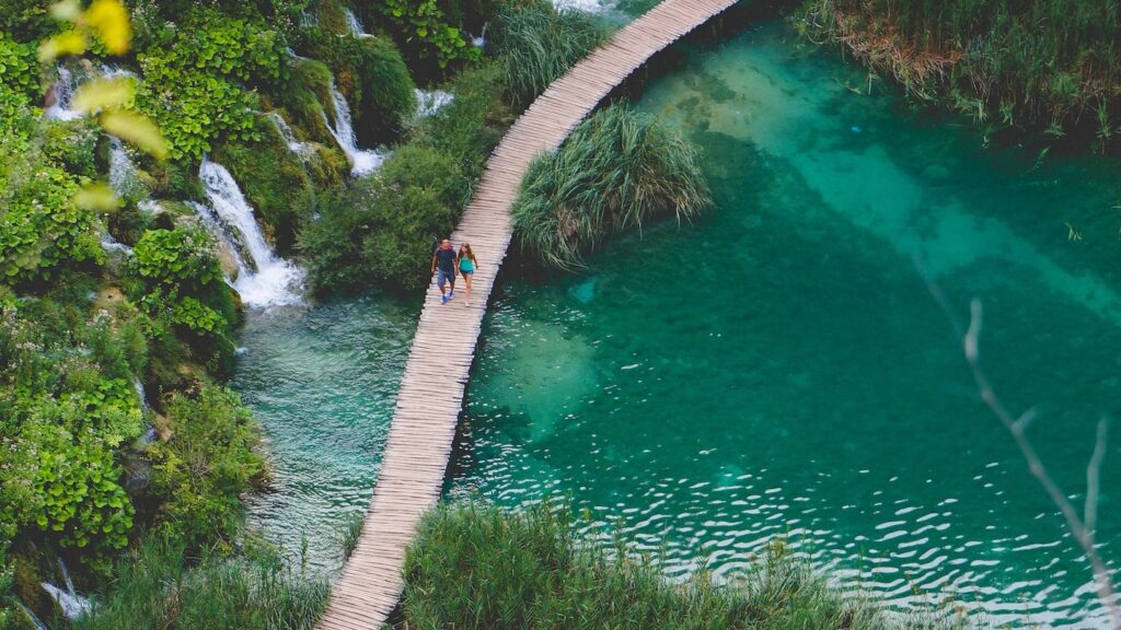 An aerial view of Plitvice Lakes National Park boardwalk, with a couple strolling hand in hand along it. 