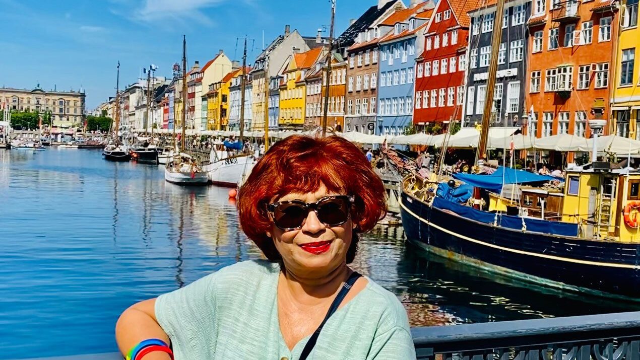 Image of Mita on tour in Copenhagen, with the colourful waterfront buildings of Nyhavn harbour in the background