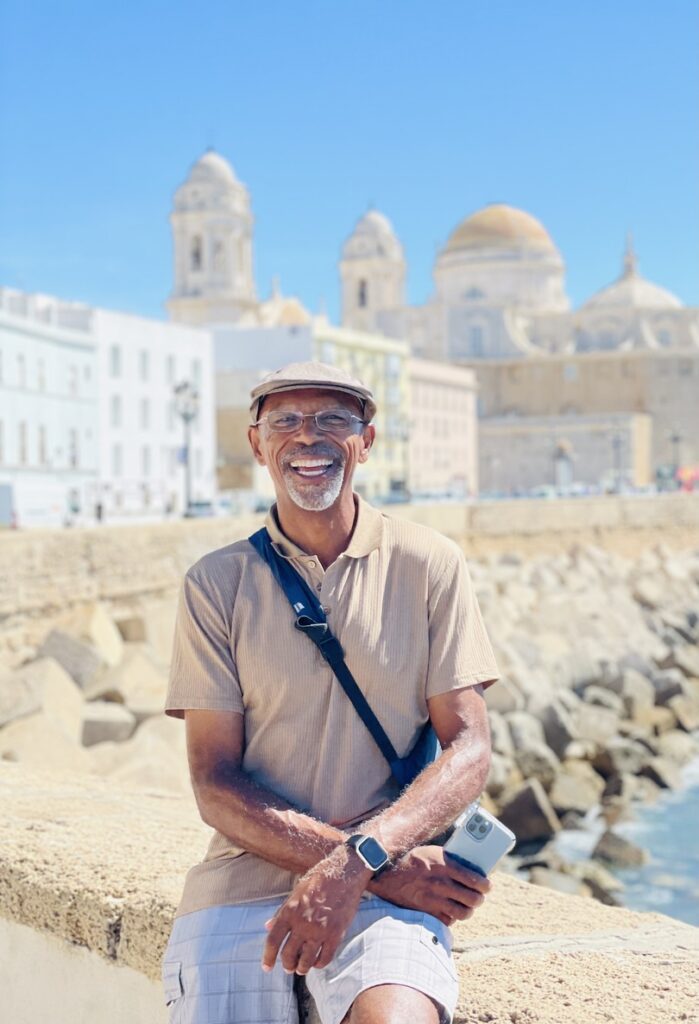 Image of Lawrence sitting on a sea wall with a Mediterranean city skyline in the background