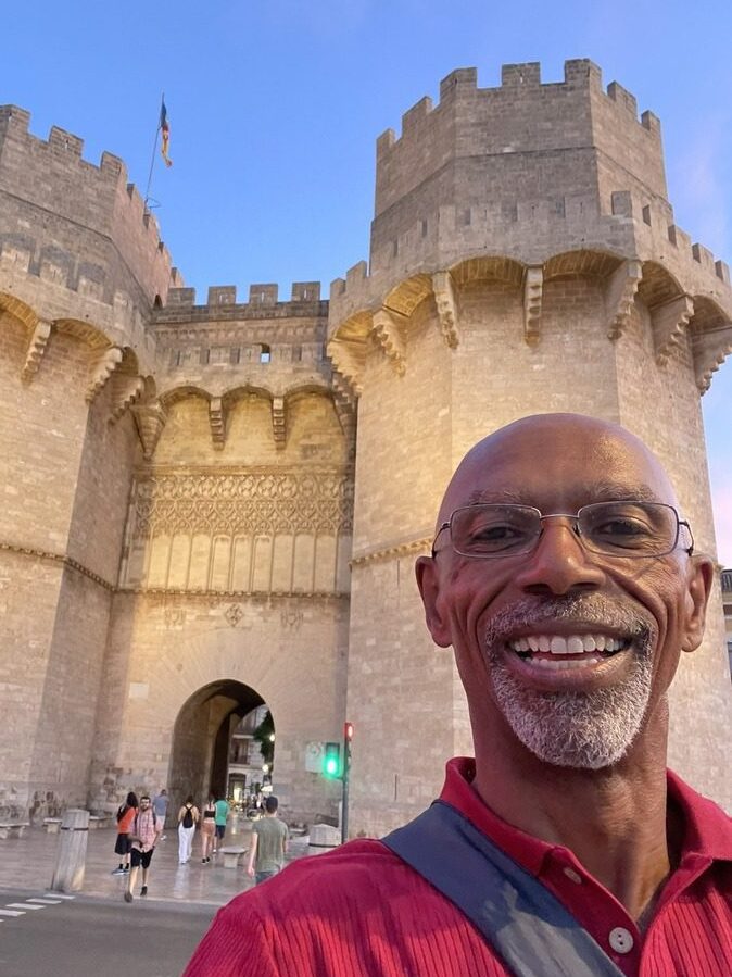 Selfie image of Lawrence with Valencia's Serranos Towers in the background, illuminated from below