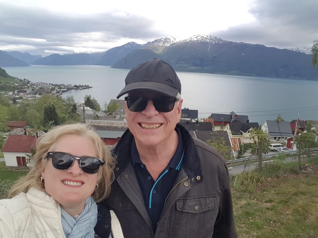 Selfie image of Leith and David in Bergen, taken from the top of a hill, with the city and fjord in the background