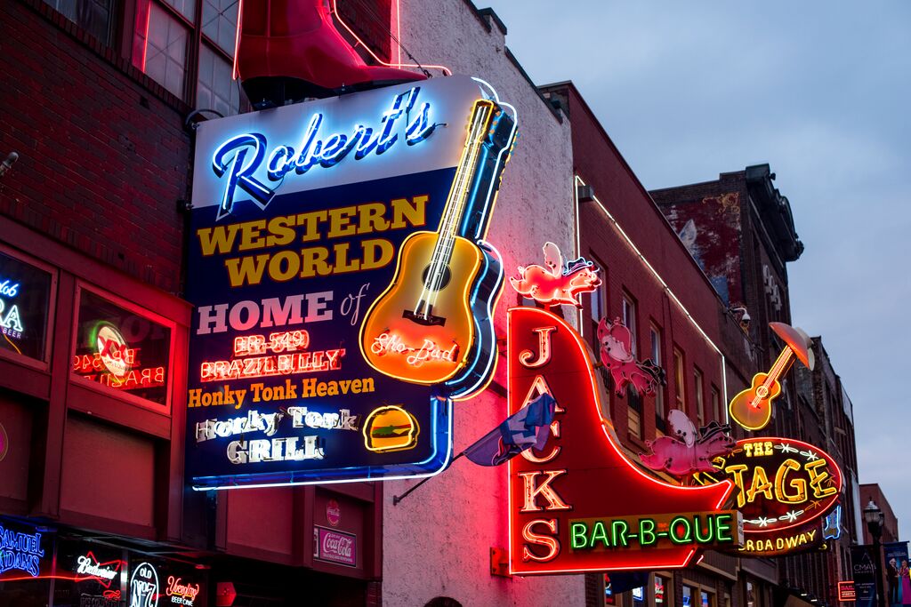 Neon signs advertising country music bars and barbecue restaurants on Broadway, Nashville at dusk during Trafalgar tours.