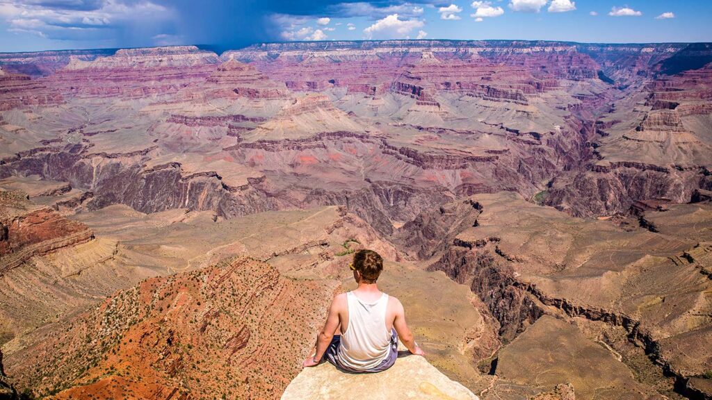 Image of a man sitting on a ledge overlooking Grand Canyon national park