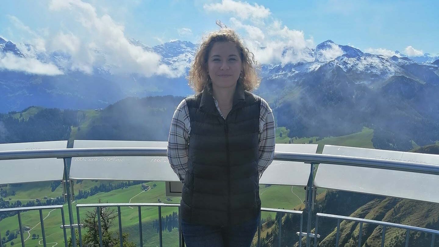 Image of Lucie, standing at a viewpoint overlooking green hills and cloud-covered mountains in Switzerland