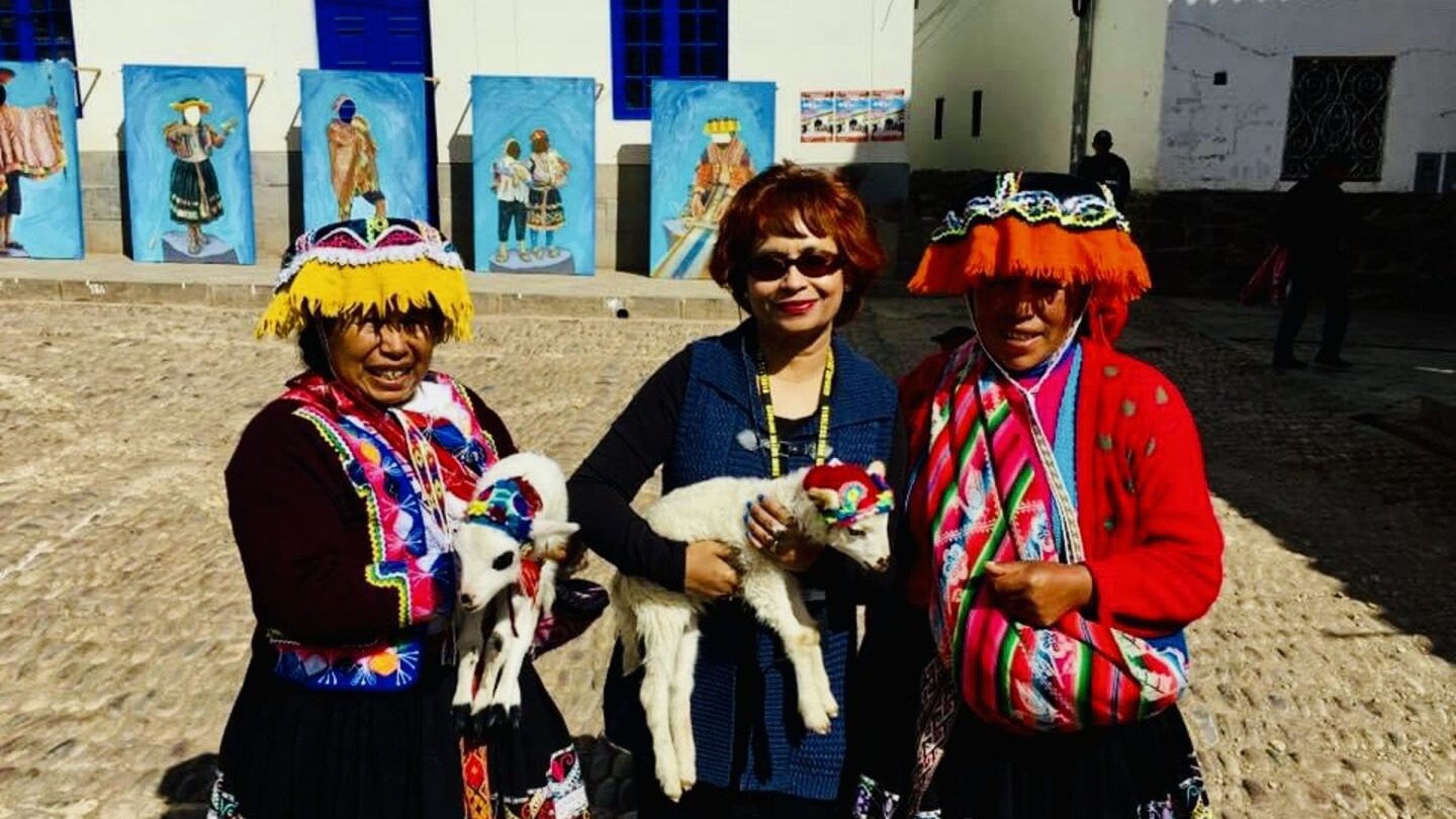 An image of Mita standing alongside brightly-dressed locals holding baby goats in Peru