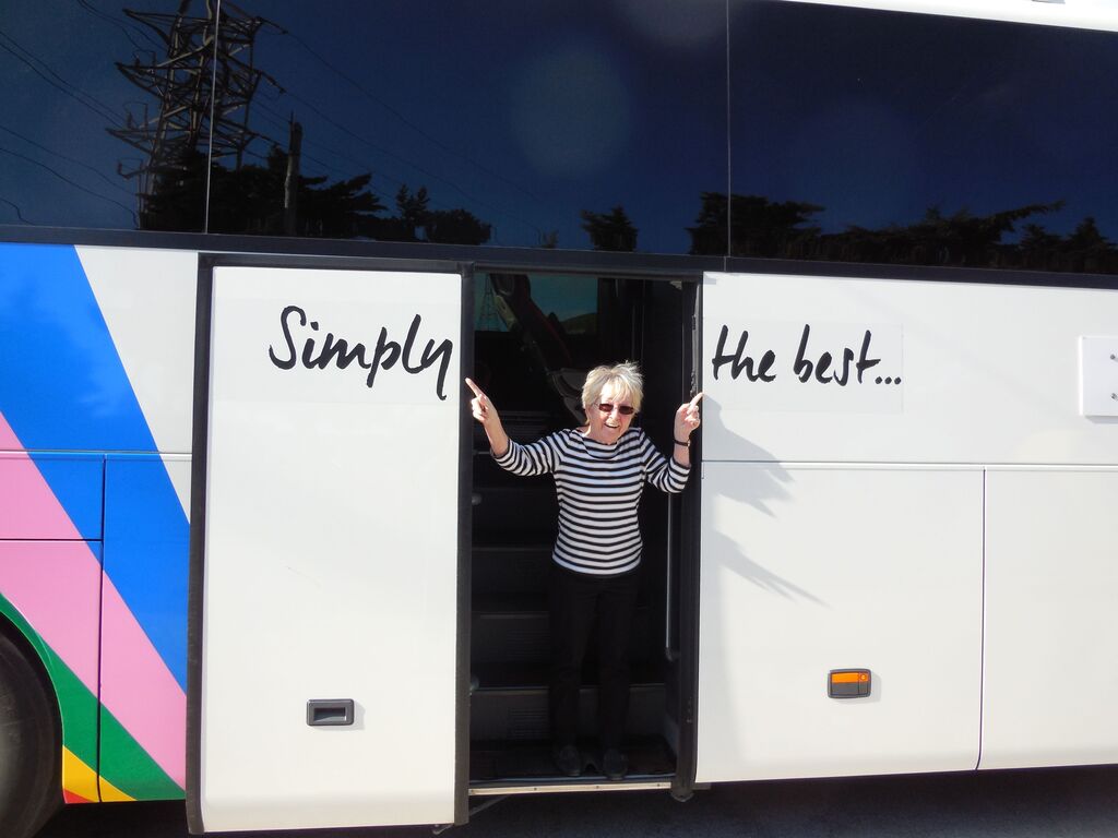 Woman posing in the door of a Trafalgar travel coach, pointing to the words 'Simply the best'