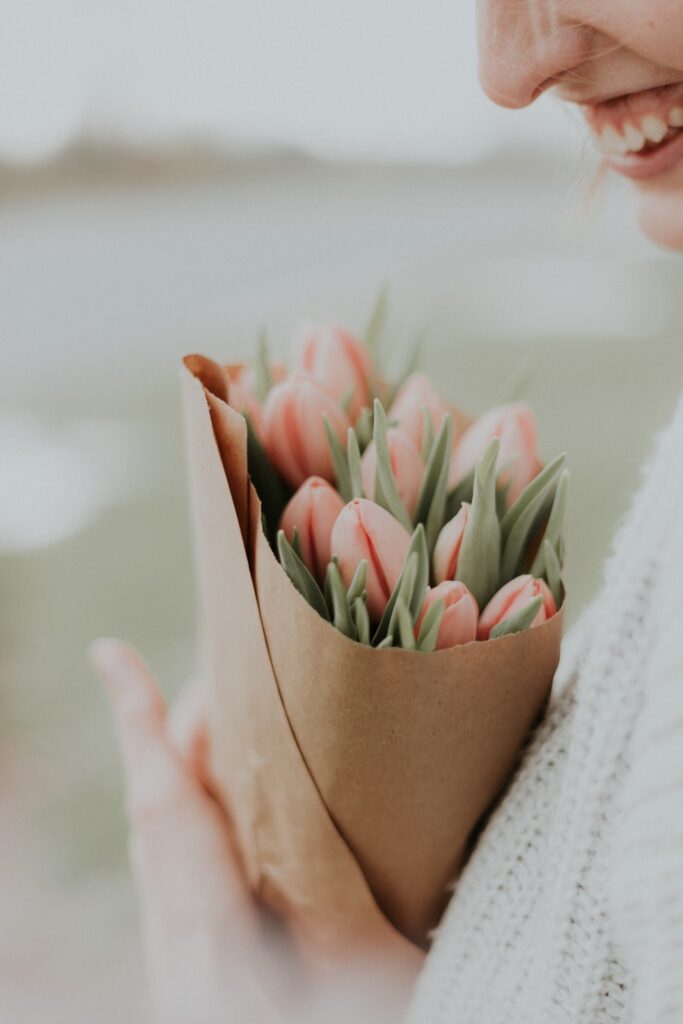 woman smiling while holding a bunch of pink flowers