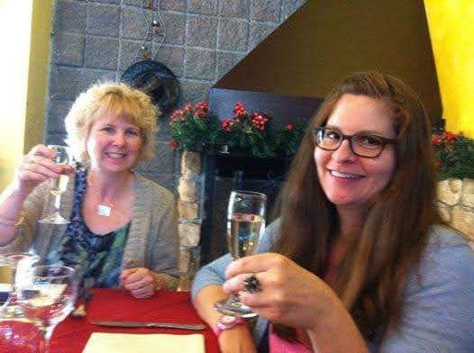 Two friends smiling and posing for a photo holding up wine flutes