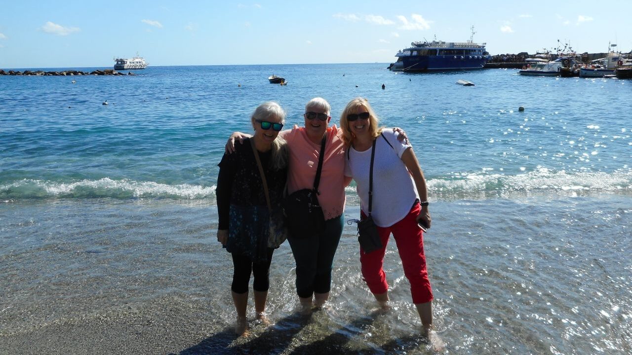 Three new friends pose for a photo in the shallow waters of a beach with the ocean behind them