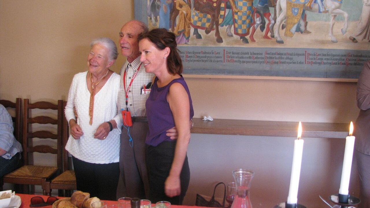 Three people pose for a photo that is being taken from a different angle. Candles light up the scene in the foreground