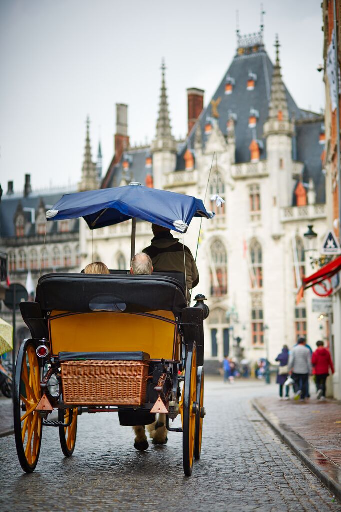 The back of a horse-drawn carriage going down a cobblestone path in Bruges.