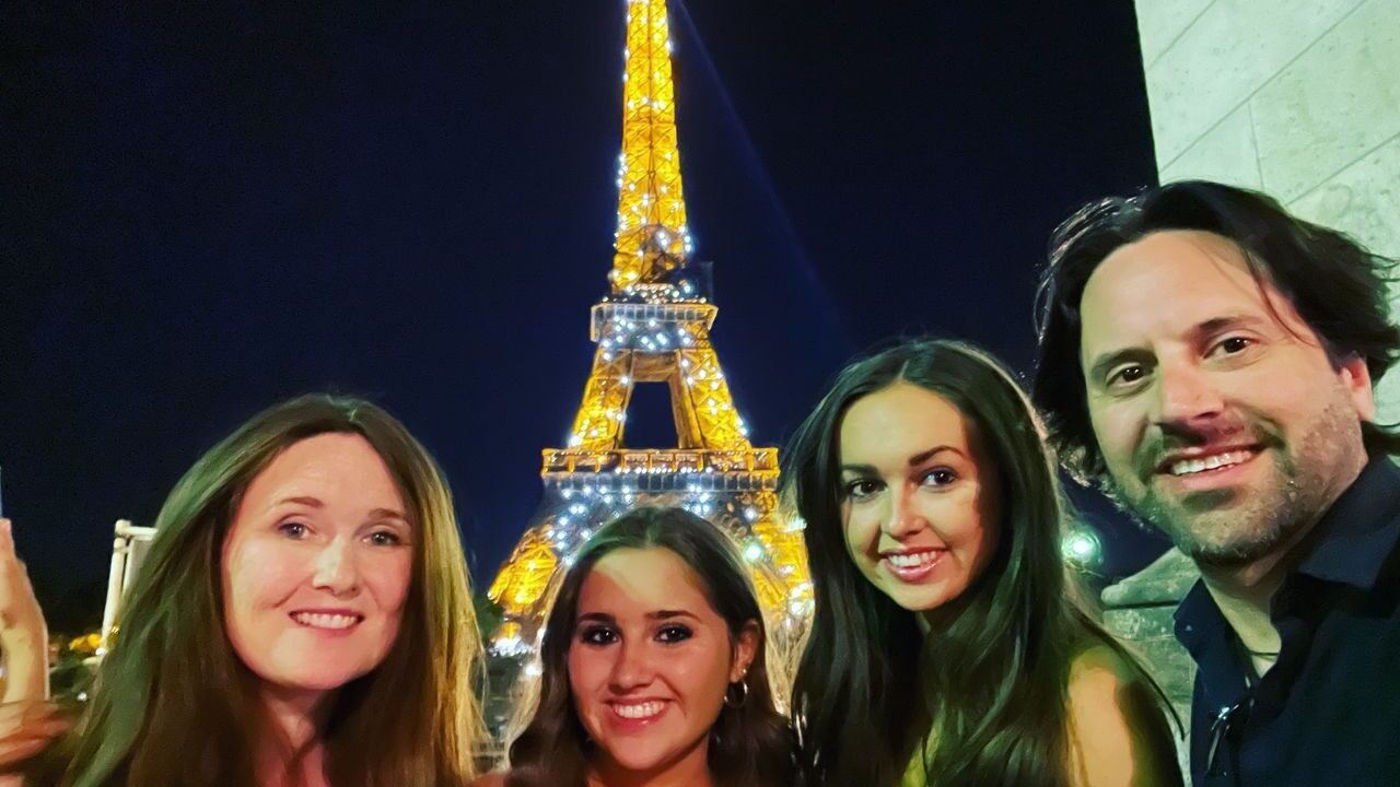 A family taking a selfie and smiling in front of the glittering Eiffel tower, making new wonderful Travel stories in Europe