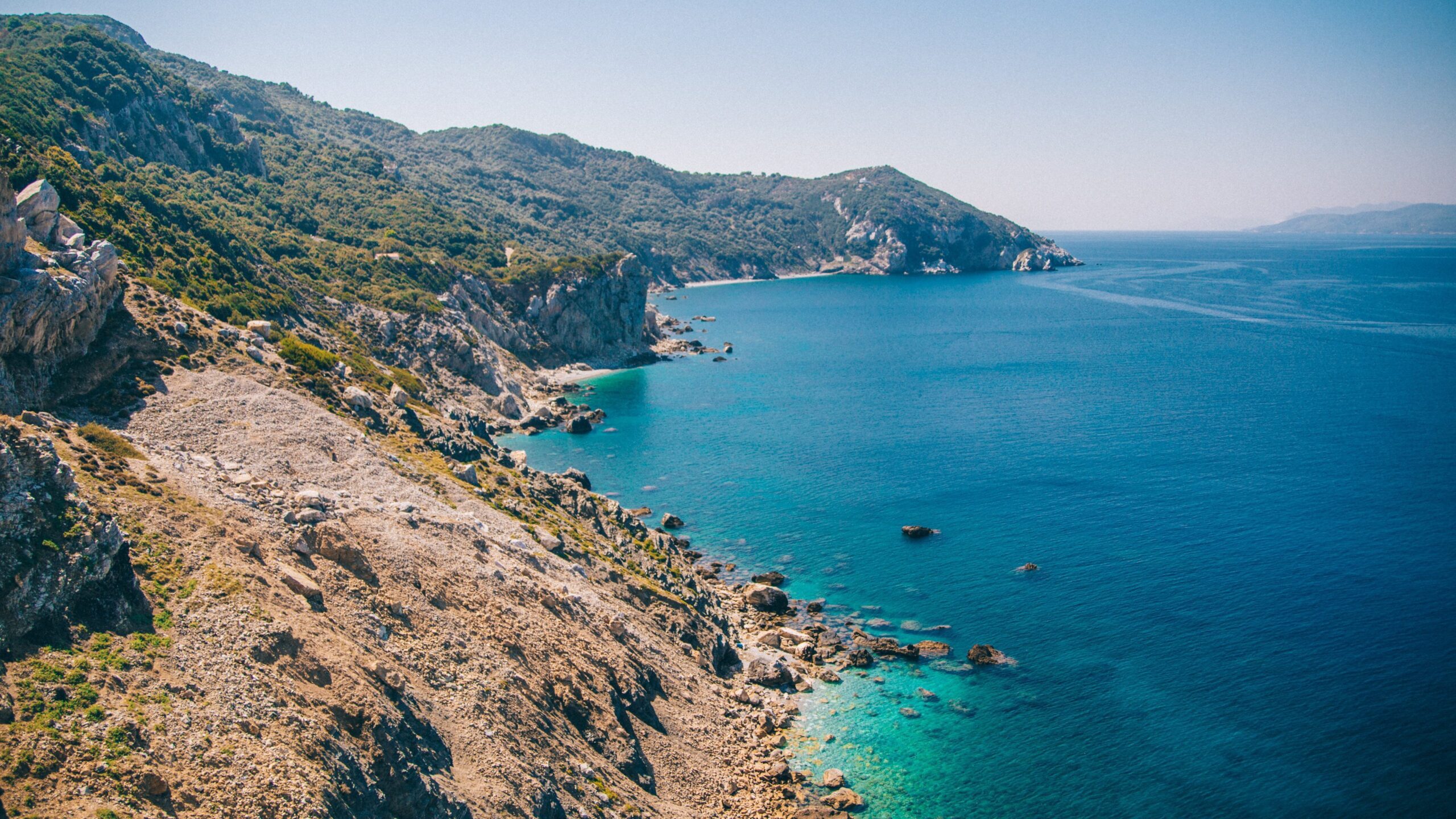 View of Skiathos' coastline; rugged cliffs sloping down towards a calm blue sea