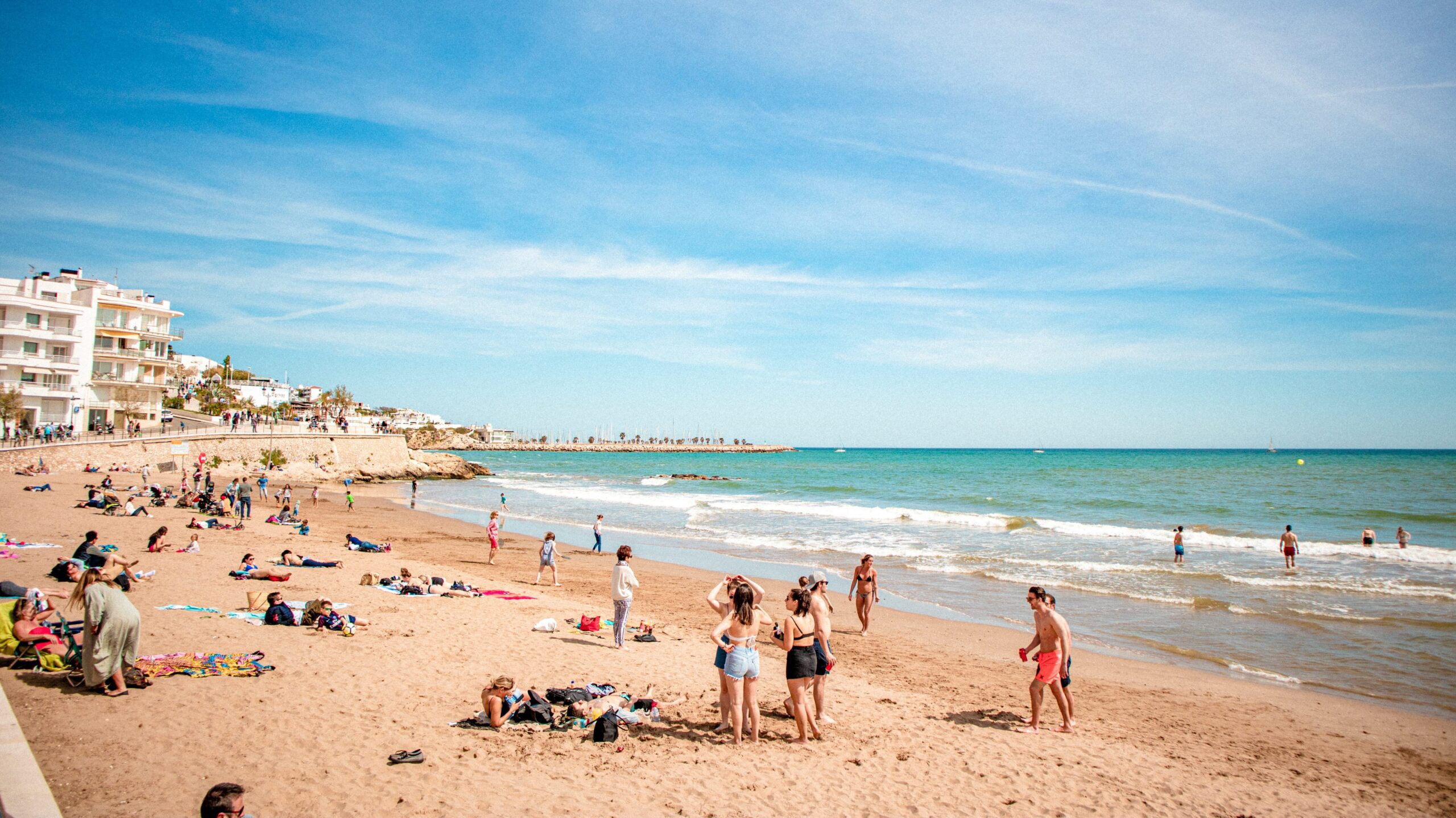 The Sitges beach, where people are relaxing in the sun next to a blue sea.