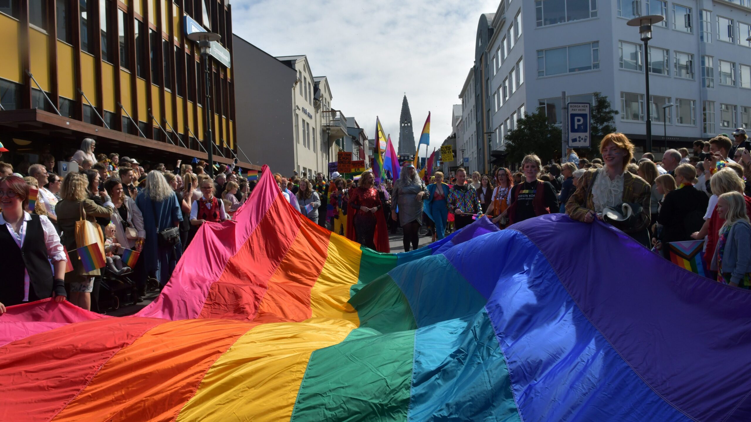 Reykjavik during Pride, where revelers hold a large Pride flag during a parade. Reykjavik is known for being one of the world's most LGBTQ friendly cities