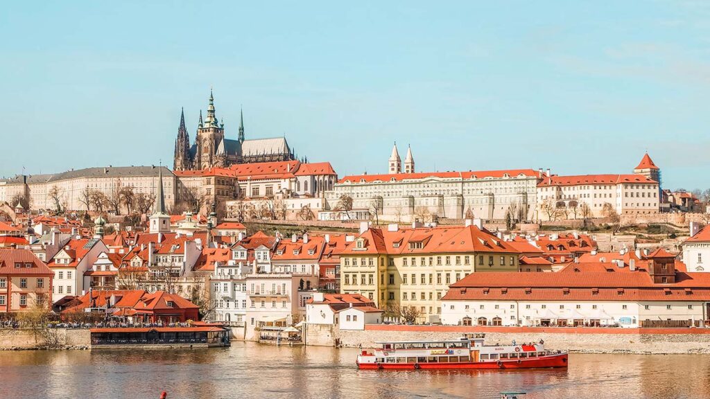 Image of Prague's St. Vitus cathedral against a blue sky, with the river Vltava in the foreground