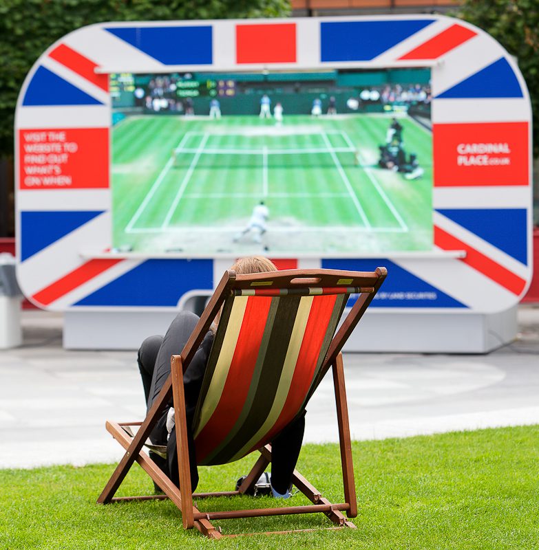Someone sitting in a colorful deckchair watching wimbledon tennis on an outdoor screening